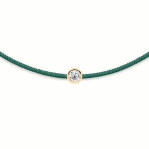 Op de afbeelding: Een armband met een enkele ronde briljant geslepen diamant in een gepolijste geelgouden zetting. De diamant is gecentreerd op een donkergroen gevlochten koord, wat zorgt voor een eenvoudig en verfijnd sieraad met een strak ontwerp.