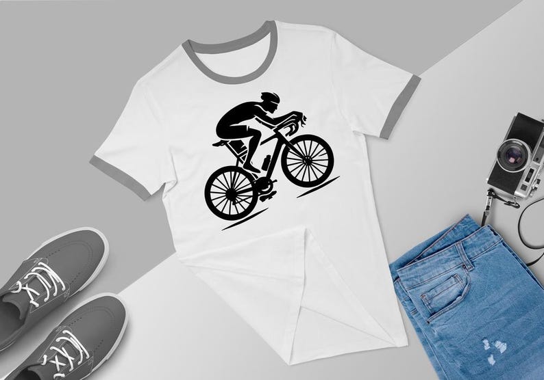 May include: White t-shirt with a black silhouette of a cyclist riding a bicycle. The t-shirt has a grey ringer.