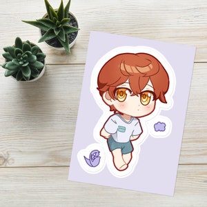 May include: A cartoon illustration of a young person with orange hair wearing a light blue shirt and blue shorts. The illustration is on a sticker with a purple flower and a cloud.