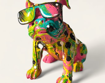 Könnte beinhalten: Eine farbenfrohe, rosafarbene, gelbe, grüne und schwarze Bulldoggenfigur mit Sonnenbrille. Die Figur ist mit einem Sprühfarbeffekt bemalt.