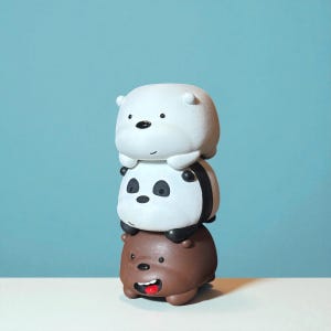 May include: A stack of three cartoon bear figurines. The top bear is white, the middle bear is panda-like with black and white markings, and the bottom bear is brown with a red mouth. The bears are stacked on top of each other against a blue background.