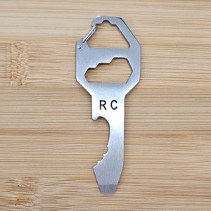 Puede incluir: Una multiherramienta de plata con forma de llave con un abridor de botellas, un bucle para sujetar a un llavero y las iniciales "RC" grabadas en el mango.