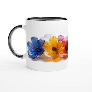 Könnte beinhalten: Weiße Keramiktasse mit schwarzem Rand, verziert mit einem farbenfrohen Blumendesign. Die Blumen sind blau, gelb, weiß und rot und in einer Reihe über die Tasse angeordnet.