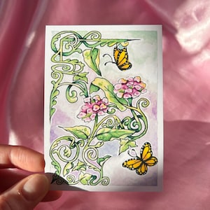 以下が含まれることがあります： 長方形のカードに描かれた水彩イラスト。ピンクの花と黄色の蝶が描かれた、装飾的な緑のデザインです。このアートワークは、紫と緑のタッチを加えた、柔らかいパステルカラーパレットです。