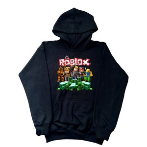 May include: Black hoodie with a graphic print of Roblox characters standing on stacks of money. The text "ROBLOX" is printed in red letters above the characters.
