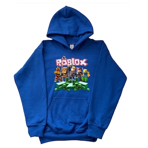 May include: A royal blue hooded sweatshirt with a graphic print of Roblox characters standing on a pile of green cash. The text "ROBLOX" is printed in red letters above the characters.