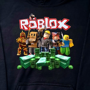 May include: Black hoodie with a graphic print of the word "ROBLOX" in red and white letters. The graphic also features cartoon characters from the game, including a knight, a robot, a builder, a pirate, and a blue character. The characters are standing on a pile of green money.