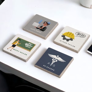 Pode incluir: Quatro  tapetes quadrados com diferentes desenhos e nomes. Os tapetes são feitos de um material cinza claro e têm uma textura áspera. Os desenhos incluem uma mulher com um laptop, uma mulher com um apontador na frente de um quadro-negro, um homem com um capacete e uma engrenagem, e um símbolo médico com uma cobra enrolada em torno de um cajado.
