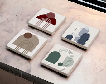Op de afbeelding: Vier vierkante onderzetters met abstracte geometrische ontwerpen. De onderzetters zijn gemaakt van een lichtbeige materiaal met een ruwe textuur. De ontwerpen bevatten verschillende kleuren, waaronder rood, bruin, groen en blauw.