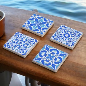 Può includere: Set di quattro sottobicchieri in ceramica blu e bianca con intricati motivi floreali. I sottobicchieri sono quadrati e hanno una superficie leggermente ruvida.