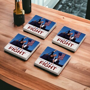 May include: Four square white coasters with a photo of three people holding an American flag. The text "FIGHT" is printed on each coaster.