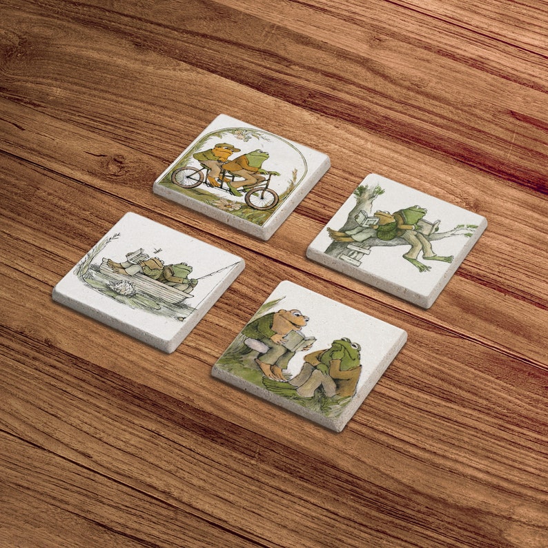Puede incluir: Cuatro posavasos cuadrados de cer&aacute;mica con ilustraciones de ranas en diversas actividades. Los posavasos representan ranas montando en bicicleta, pescando, leyendo y sentadas en una rama de &aacute;rbol.