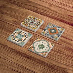 Puede incluir: Cuatro posavasos cuadrados de cer&aacute;mica con intrincados dise&ntilde;os florales en tonos azules, verdes, amarillos y naranjas. Los posavasos est&aacute;n colocados sobre una superficie de madera.