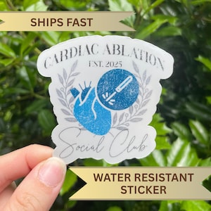 May include: A water-resistant sticker with the text "CARDIAC ABLATION Social Club" and a blue heart illustration. The sticker also features the text "EST. 2025" and an image of a medical tool. The sticker is held by a hand.