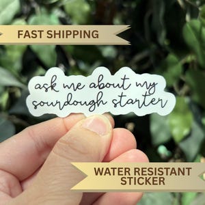 May include: A white die-cut sticker with a wavy, cloud-like border featuring the black cursive text "ask me about my sourdough starter" printed in the center. The sticker has a smooth finish and is shaped to follow the text.