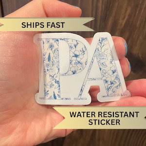May include: A white sticker with the letters "PA" in blue outlined letters. The letters are filled with a blue and white floral pattern. The sticker has the text "SHIPS FAST" and "WATER RESISTANT STICKER" on either side.