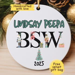 May include: A white ceramic ornament with the name "Lindsay Peepa" in green letters. The letters "BSW" are in black, with illustrations of a mouse, ballet shoes, a nutcracker, and a drum. A small Christmas tree and the year 2025 are also featured.