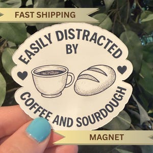 May include: A white magnet with the text "EASILY DISTRACTED BY COFFEE AND SOURDOUGH" in a circular design. The design includes a coffee cup, a loaf of bread, and two heart shapes. The words "FAST SHIPPING" and "MAGNET" are also visible.
