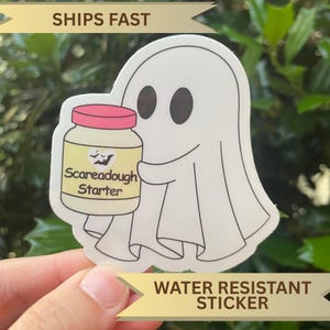 May include: A white ghost sticker holding a jar labelled "Scareadough Starter." The jar has a pink lid and a yellow label with a bat design. The sticker is water resistant.