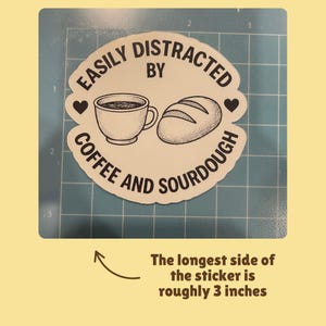 May include: A white sticker with the text "EASILY DISTRACTED BY COFFEE AND SOURDOUGH" surrounds a coffee cup and a loaf of bread. The longest side of the sticker is roughly 3 inches.