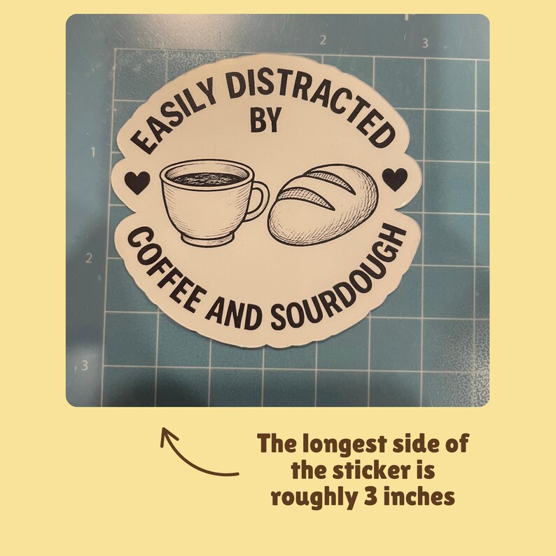 May include: A white sticker with the text "EASILY DISTRACTED BY COFFEE AND SOURDOUGH" surrounds a coffee cup and a loaf of bread. The longest side of the sticker is roughly 3 inches.