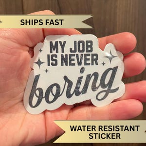 May include: White sticker with black text that reads "My job is never boring" with two small stars on either side of the text. The sticker has a silver glitter finish.