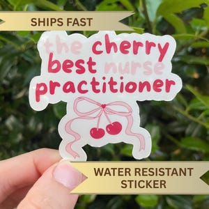 以下が含まれることがあります： ピンクと赤で「the cherry best nurse practitioner」と書かれた白いステッカー。ステッカーは、リボンと2つのさくらんぼが付いたさくらんぼのデザインが特徴です。ステッカーは耐水性です。