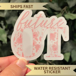 May include: A white sticker with the words "future OT" in pink script. The letters "O" and "T" are filled with a pink floral pattern. The sticker is water resistant.