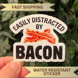May include: A white, water-resistant sticker with the text "EASILY DISTRACTED BY BACON". The sticker features a graphic of cooked bacon. The words "FAST SHIPPING" and "WATER RESISTANT STICKER" are also visible.
