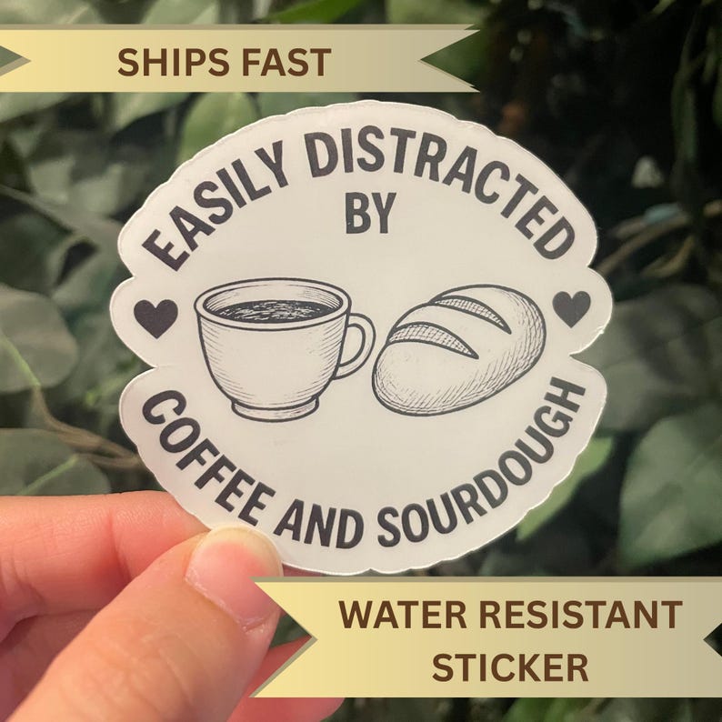 May include: A white sticker with the text "EASILY DISTRACTED BY COFFEE AND SOURDOUGH" in a circular design. The design includes a coffee cup, a loaf of bread, and two hearts. The sticker also says "WATER RESISTANT STICKER".