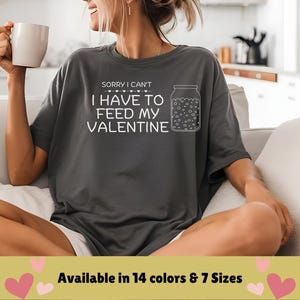 Può includere: Una maglietta grigia con il testo "SORRY I CAN'T I HAVE TO FEED MY VALENTINE" e un disegno di un barattolo con cuori all'interno. Disponibile in 14 colori e 7 taglie.
