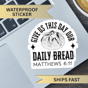 May include: Black and white sticker with the text "Give us this day our daily bread Matthew 6:11" and a drawing of a loaf of bread.