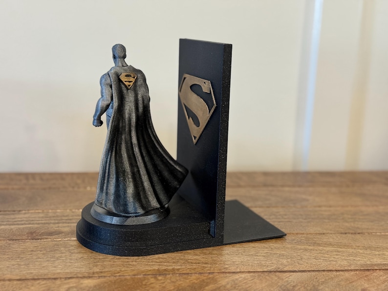 May include: A black and gray Superman bookend set. One bookend features a Superman figure with a cape and the Superman logo on the back. The other bookend is a black rectangular shape with the Superman logo.