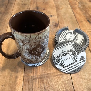 May include: A brown ceramic mug with a graphic of the Marauder's Map from the Harry Potter series. The mug is sitting on a gray coaster with a car design. There are three additional coasters with the same design.