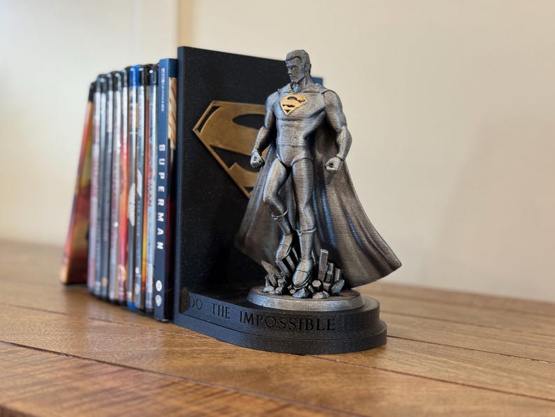May include: A Superman-themed bookend set. The set includes a black bookend with a gold Superman logo and a silver Superman figure. The base of the bookend reads "DO THE IMPOSSIBLE". A collection of books is held in place.