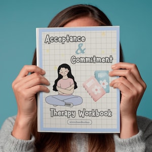 May include: A person holds a workbook titled "Acceptance & Commitment Therapy Workbook". The cover illustration shows a meditating person, two small notebooks, and the text "Acceptance & Commitment". The background has a grid pattern.