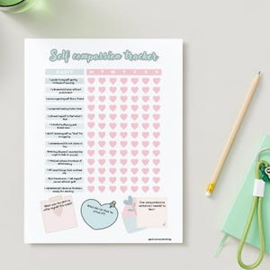 May include: A white self-compassion tracker sheet with a mint green title and pink heart-shaped boxes. The tracker includes prompts for daily habits and space for notes. A pencil and a green notebook are in the background.