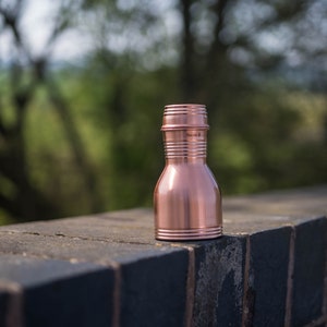 May include: A copper water bottle with a traditional design. The bottle is sitting on a brick wall.