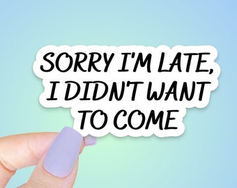 May include: White sticker with the text "Sorry I'm late, I didn't want to come" in black lettering. A hand is holding the sticker.