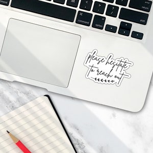 May include: A white laptop computer with a black keyboard and a sticker that says "Please hesitate to reach out" with a small line of leaves underneath the text.