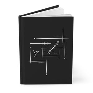 Op de afbeelding: Een zwart notitieboek met een wit abstract geometrisch ontwerp op de omslag. Het ontwerp bevat lijnen, stippen en vormen. Het notitieboek is open en toont witte pagina's.
