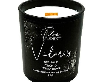 May include: A black candle in a glass jar with a white wax top and a wooden wick. The label features the text Poe Candle Co. Velaris, Sea Salt, Orchid, Tonka Bean, Hand Poured Vegan Candle, 9 oz. The design includes white abstract accents.