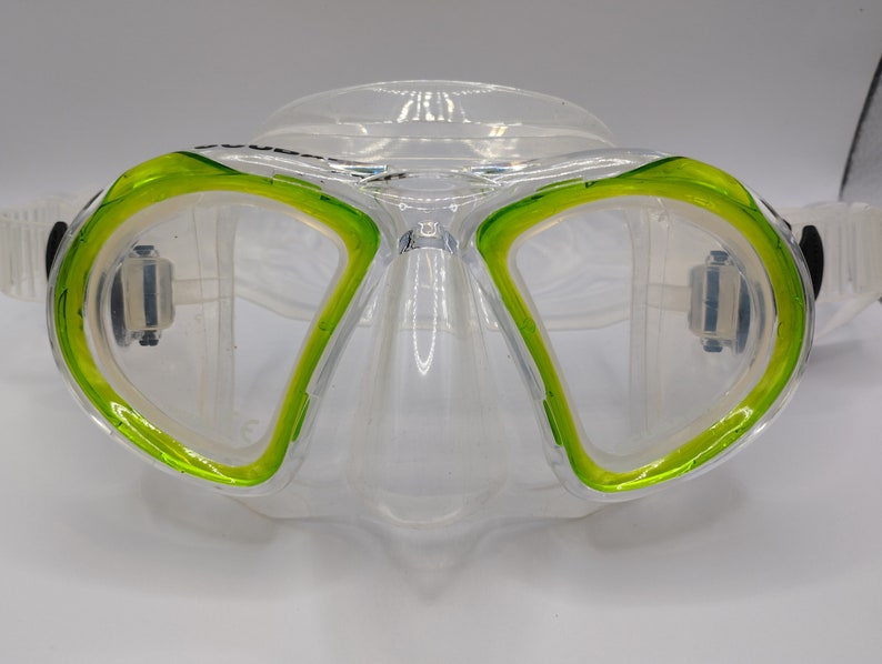 Op de afbeelding: Een helder duikmasker met een groene siliconen rok. Het masker heeft een heldere lens en een neuszak.