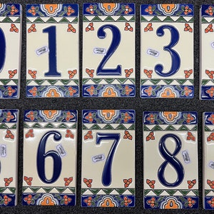 May include: Ten ceramic tiles with a traditional Mexican design. Each tile features a different number from 0 to 9 in blue on a cream background. The tiles have a green, blue, and orange border with floral patterns.