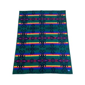 May include: A rectangular blanket featuring a dark green base with a repeating geometric pattern in black. The design includes horizontal bands of rainbow-colored stripes in red, orange, yellow, and blue, creating a vibrant contrast against the green.