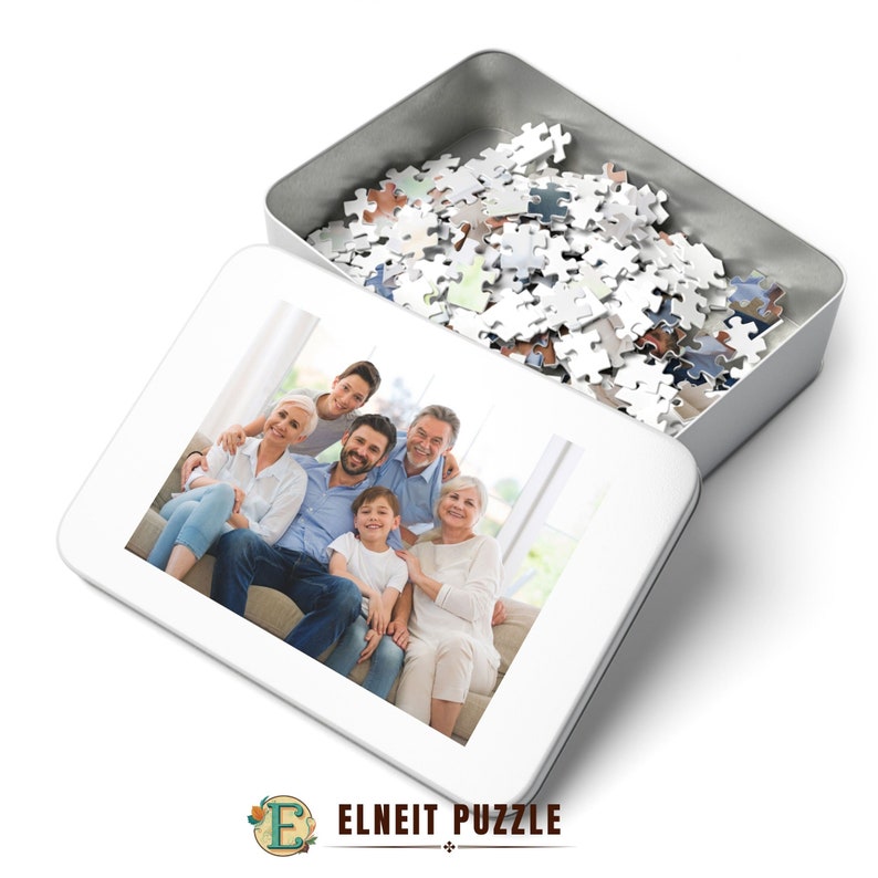 K&ouml;nnte beinhalten: Eine wei&szlig;e Metallbox mit offenem Deckel, die ein wei&szlig;es Puzzle enth&uuml;llt. Die Box hat ein Foto auf der Vorderseite von einer sechsk&ouml;pfigen Familie, die l&auml;chelnd auf einem Sofa sitzt.