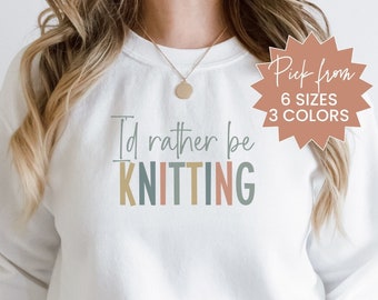 May include: White sweatshirt with the text "I'd rather be KNITTING" in pastel colors. The sweatshirt has a crew neck and long sleeves. A tag in the upper right corner says "Pick from 6 sizes 3 colors".