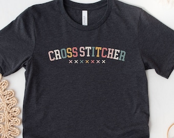 May include: Dark grey heather t-shirt with the text "CROSS STITCHER" in colorful letters. The text is in a retro style font.