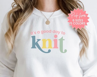 May include: White sweatshirt with the text "it's a good day to knit" in colorful letters. The word "knit" is in a stylized font with each letter in a different color.