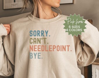 May include: A beige sweatshirt with the text "SORRY. CAN'T. NEEDLEPOINT. BYE." in colorful letters. The sweatshirt is available in 6 sizes and 4 colors.